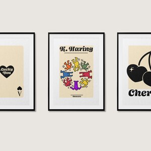 May include: Three framed prints with a minimalist design. The left print features a black ace of spades playing card with the text "lucky you". The middle print features a black and white illustration of dancing figures in a circle with the text "K. Haring" and "©1980s". The right print features a black silhouette of two cherries with a green stem and the text "Cherry".