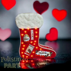 May include: A red stocking with a white fur trim, filled with chocolate and sweets. The stocking is decorated with small red hearts and lights. The background is a wall with red hearts.