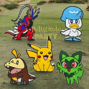May include: Five colourful cartoon character cutouts, including a red and blue dragon, a yellow Pikachu, a green cat-like creature, a brown dinosaur-like creature, and a white duck with a blue hat. The cutouts are on a green grassy surface.