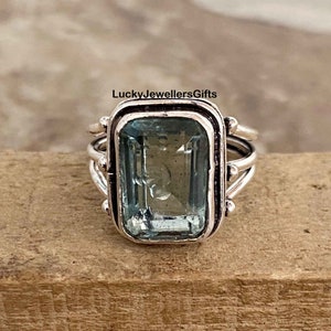 Könnte beinhalten: Ein silberner Ring mit einem hellblauen Aquamarin-Edelstein im Smaragdschliff. Der Ring hat ein schlichtes Band mit einem zarten Design.