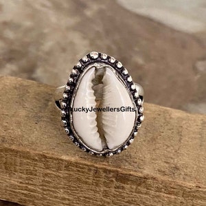 May include: A silver ring featuring a white seashell design. The ring is adorned with a beaded border.