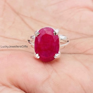 Könnte beinhalten: Ein Silberring mit einem großen, oval geschliffenen, tief rosa-roten Edelstein, der von vier Krappen gehalten wird. Die Ringschiene ist aus poliertem Silber und der Text LuckyJewellersGifts ist links neben der Ringfassung zu sehen.