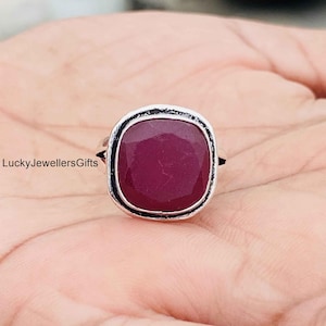 May include: A silver ring featuring a large, square-shaped, faceted deep pink gemstone with rounded corners. The metal band has a dark, oxidized finish around the setting. The text LuckyJewellersGifts is visible on the left side of the image.