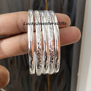 May include: Five silver bangles with a hammered texture. The bangles are stacked on top of each other. The text "LuckyJewellersGifts" is visible in the image.