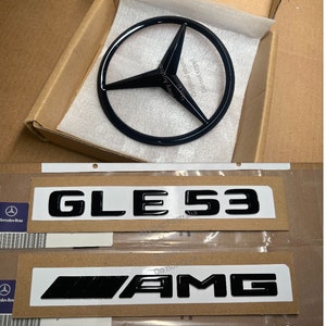May include: Black Mercedes-Benz emblem with a three-pointed star in a circle, and two black plastic emblems with the text "GLE 53" and "AMG" on a brown background.