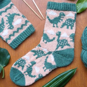 Peut inclure: Une paire de chaussettes en tricot vert et rose avec un motif de dinosaure. Les chaussettes sont faites avec un fil doux et ont une coupe confortable.