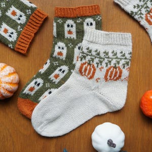 Puede incluir: Calcetines tejidos a mano con dise&ntilde;os de Halloween. Un par presenta patrones de fantasmas verdes y blancos, mientras que otro muestra calabazas naranjas y follaje verde. Los calcetines tienen pu&ntilde;os y talones naranjas y blancos, perfectos para el oto&ntilde;o.