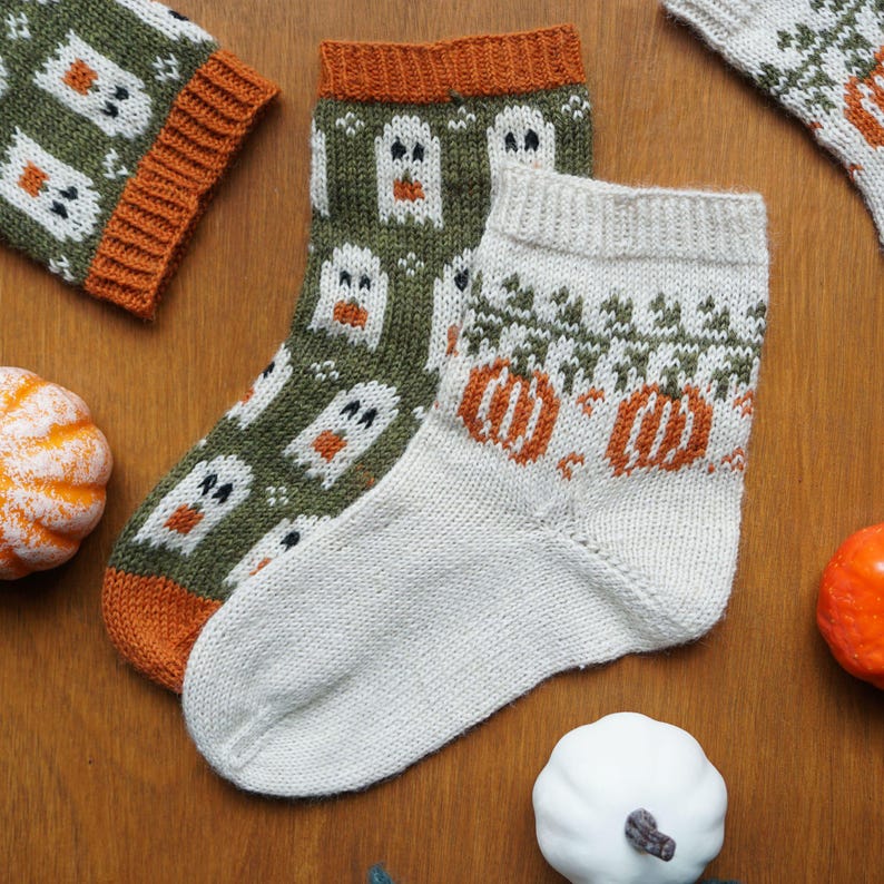 Puede incluir: Calcetines tejidos a mano con dise&ntilde;os de Halloween. Un par presenta patrones de fantasmas verdes y blancos, mientras que otro muestra calabazas naranjas y follaje verde. Los calcetines tienen pu&ntilde;os y talones naranjas y blancos, perfectos para el oto&ntilde;o.