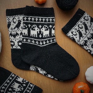 May include: A pair of black socks with a white Nordic-style pattern. The design includes stylized animal and geometric motifs. The socks are made of a thick, knitted material, ideal for keeping feet warm during the colder months.