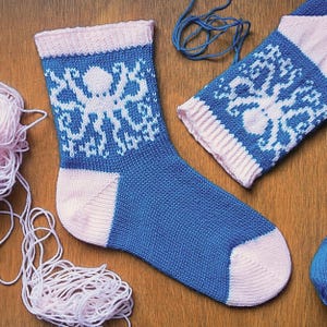 May include: A pair of knitted socks featuring a blue and white octopus pattern. The socks have a light pink ribbed cuff, a light pink heel, and a light pink toe section. The main body of the socks is blue with a white octopus motif.