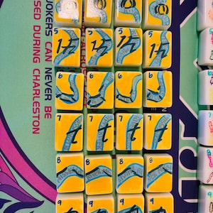May include: A set of rectangular mahjong tiles with a yellow background and a blue river graphic. Each tile features a black number from 4 to 9 and the text Mississippi River. The tiles are arranged in rows on a mat with the text JOKERS CAN NEVER BE PASSED DURING CHARLESTON.