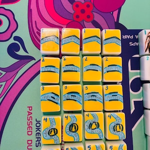 May include: A set of rectangular mahjong tiles arranged in a grid, featuring a yellow background with blue river-like illustrations and the text Mississippi River. Each tile is numbered one through five in the top left corner in blue ink.