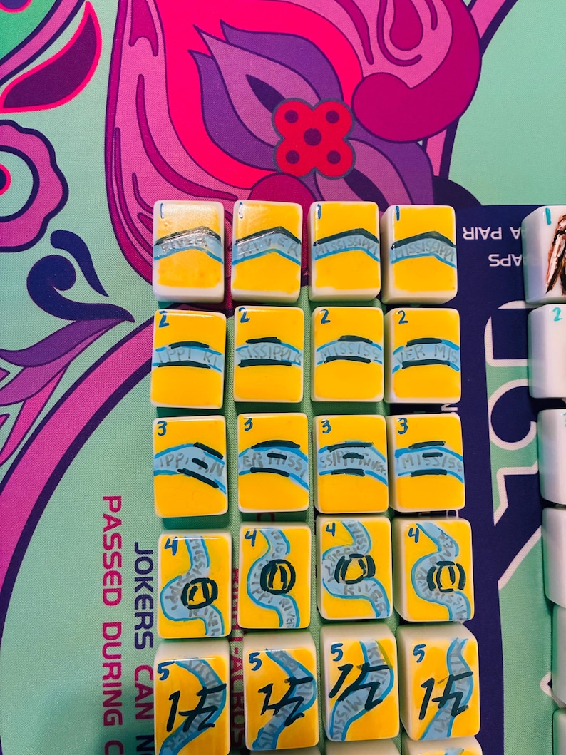 May include: A set of rectangular mahjong tiles arranged in a grid, featuring a yellow background with blue river-like illustrations and the text Mississippi River. Each tile is numbered one through five in the top left corner in blue ink.