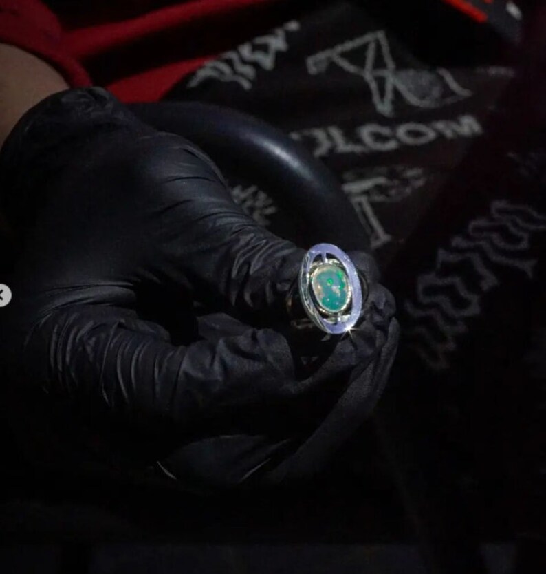 May include: A silver ring with a green oval gemstone set in a silver bezel. The ring is surrounded by a silver band with a textured design.
