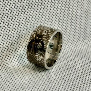 Pu&ograve; includere: Un anello d'argento con una fascia a motivi bianco e nero. Il motivo &egrave; un design a spirale.