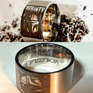 Pu&ograve; includere: Un anello d'argento con le parole "The Bounty Hunter" e "DURAN" incise. L'anello presenta anche un'immagine stilizzata di un elmetto mandaloriano.