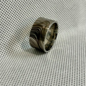 Pu&ograve; includere: Una fascia larga d'argento con un motivo a spirale bianco e nero. La fascia &egrave; liscia e lucida.