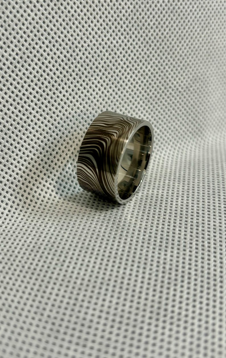 Pu&ograve; includere: Una fascia larga d'argento con un motivo a spirale bianco e nero. La fascia &egrave; liscia e lucida.