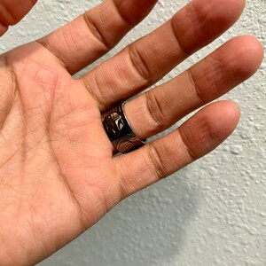 Pu&ograve; includere: Un anello d'argento con un designo in bianco e nero che presenta il viso di un personaggio e la parola "DOUNT".