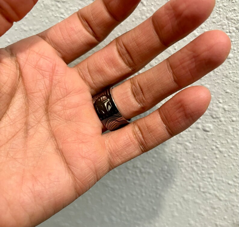 Pu&ograve; includere: Un anello d'argento con un designo in bianco e nero che presenta il viso di un personaggio e la parola "DOUNT".