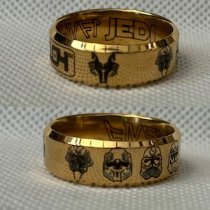 May include: Two gold-colored rings with black engravings. The top ring has the text "SWAT JEDI" and a wolf head design. The bottom ring has the text "CLONE" and four different helmet designs.