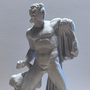 May include: A gray statue of a muscular male figure, possibly a classical god or hero, with a cloth draped over his shoulder. The statue is standing on a rectangular base and has detailed facial features and hair.