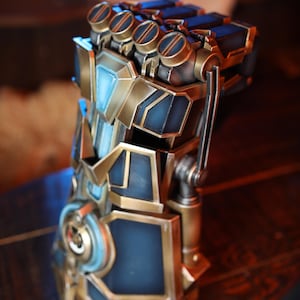 Puede incluir: Una réplica detallada del Guantelete del Infinito del Universo Cinematográfico Marvel. El guantelete está hecho de metal y tiene un esquema de color azul y dorado. El guantelete tiene seis Gemas del Infinito, cada una de un color diferente.