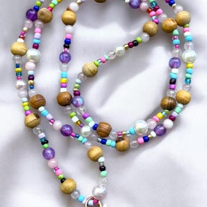 May include: A colourful beaded lanyard featuring wooden, iridescent, and pearl-like beads. The lanyard has a gold-coloured clasp and key ring. The beads are arranged in a layered design, creating a vibrant and eye-catching accessory.
