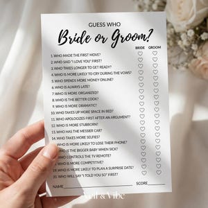 Op de afbeelding: Een witte spelkaart met de tekst "Guess Who Bride or Groom?" in zwart schrift. De kaart heeft een lijst met vragen met vakjes om antwoorden aan te kruisen. De onderkant van de kaart luidt "Veil & Vibe".