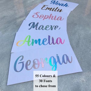 May include: Six rectangular white cards featuring custom names in various styles and colours. The names displayed are Noah in blue, Emily in brown, Sophia in pink, Maeve in dark glitter, Amelia in rainbow gradient, and Georgia in iridescent blue.