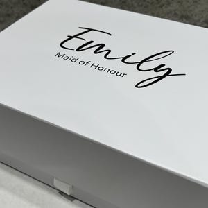May include: White gift box with a black inscription that reads "Emily Maid of Honour".