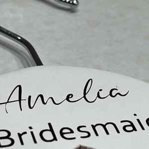 May include: White hanger with the name Amelia and the word Bridesmaid written in black lettering.