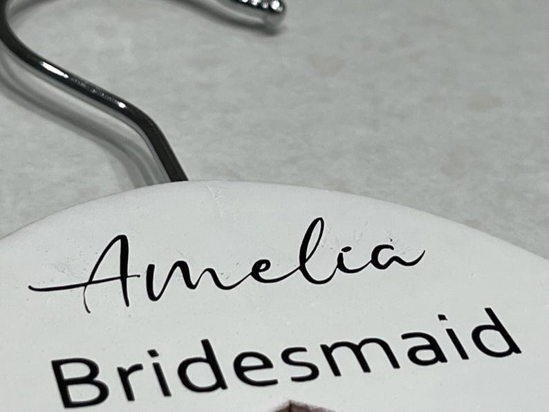 May include: White hanger with the name Amelia and the word Bridesmaid written in black lettering.