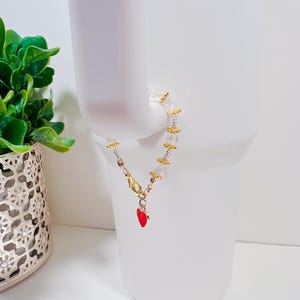May include: A delicate bracelet with clear beads and gold accents. A small red heart charm hangs from the clasp.
