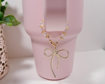 May include: A gold bow charm with clear beads attached to a pink tumbler.