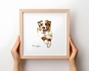 May include: A square wooden frame containing a watercolor painting of a brown and white Australian Shepherd dog with its tongue out. The name Brooklyn is written in black cursive script below the dog on the white background of the print.