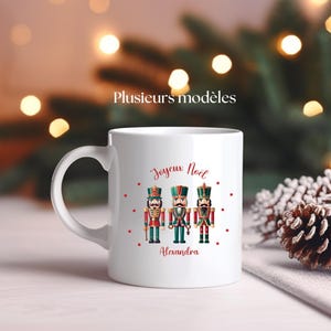 Peut inclure: Mug en céramique blanche avec un motif de Noël représentant trois casse-noisettes. Le mug porte l'inscription "Joyeux Noël" et "Alexandra".