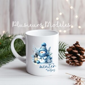 Peut inclure: Une tasse en céramique blanche avec un bonhomme de neige bleu tenant une lanterne et le texte "winter vibes" imprimé dessus.