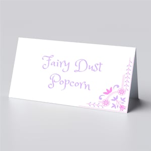 Puede incluir: Una tarjeta blanca con el texto "Fairy Dust Popcorn" en letra cursiva morada. La tarjeta tiene un diseño floral rosa y morado en la esquina.