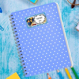 May include: A blue notebook with white polka dots and a colorful sticker with the text "Peter Jones Grade 3" and a cartoon superhero image.