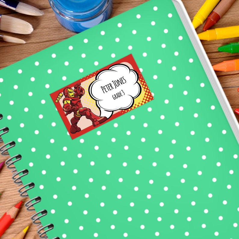 May include: A green notebook with white polka dots and a red and yellow comic book style name tag. The name tag features a cartoon superhero and the text "Peter Jones Grade 3".