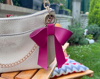 May include: A white handbag with a gold chain strap and a pink bow keychain.