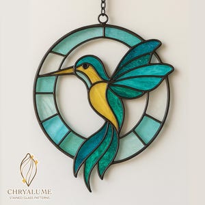 May include: Stained glass hummingbird artwork. The bird is made of yellow and teal glass, set within a teal and black circular frame. It hangs from a chain. The text "CHRYALUME STAINED GLASS PATTERNS" is displayed at the bottom.