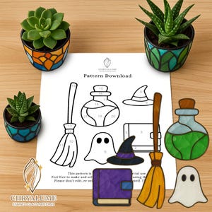 Può includere: Immagine di natura morta con tre piccole piante grasse in vaso e un foglio di download di modelli. Il foglio mostra disegni a tratteggio di modelli di vetrate a tema Halloween, tra cui un cappello da strega, una bottiglia di pozione e una scopa.