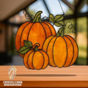 May include: Stained glass pumpkin decoration with three pumpkins of different sizes, green leaves and stems. The pumpkins are orange with black outlines, suspended by a chain. The logo "CHRYALUME STAINED GLASS PATTERNS" is at the bottom.