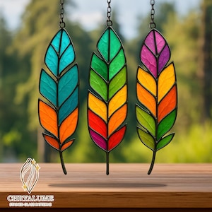 Pode incluir: Três ornamentos de penas de vitral em cores vibrantes: turquesa, laranja, verde, amarelo, vermelho e roxo. Cada pena é delineada em preto e suspensa por uma corrente. O logotipo "CHRYALUME STAINED GLASS PATTERNS" está na parte inferior.