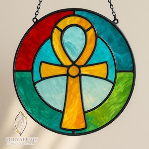 May include: Round stained glass window featuring an Ankh symbol in yellow and blue, surrounded by red, green, and teal sections. The window is framed in black and hangs from a chain. The logo "CHRYALUME STAINED GLASS PATTERNS" is at the bottom.