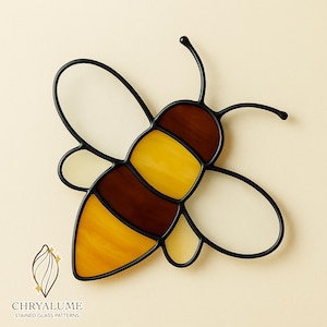 Op de afbeelding: Een gebrandschilderde bij met een zwarte metalen omtrek. Het lichaam van de bij is gesegmenteerd met amber, geel en bruin glas. De vleugels zijn helder. Het logo "CHRYALUME STAINED GLASS PATTERNS" staat in de linker benedenhoek.