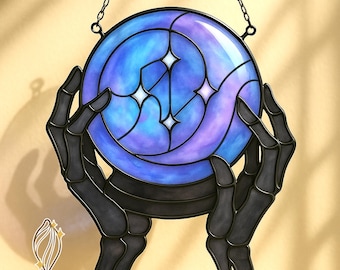 Puede incluir: Obra de arte en vidrio manchado que representa un orbe azul y púrpura con detalles de estrellas, sostenido por manos esqueléticas negras. La pieza está suspendida por una cadena y tiene el texto "CHRYALUME STAINED GLASS PATTERNS" en la parte inferior.
