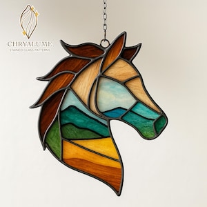 May include: Stained glass horse head with a mountain landscape design. The artwork features shades of brown, green, blue, and yellow, with a black metal frame. The piece is suspended by a chain and includes the text "CHRYALUME STAINED GLASS PATTERNS".